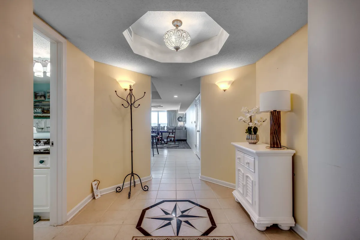 The inviting entrance foyer of the condo, featuring an octagonal ceiling light, star-patterned floor tile, a white console table with fresh flowers, and a coat rack. The scene is warm and welcoming, suggesting the first impression guests receive when arriving.
