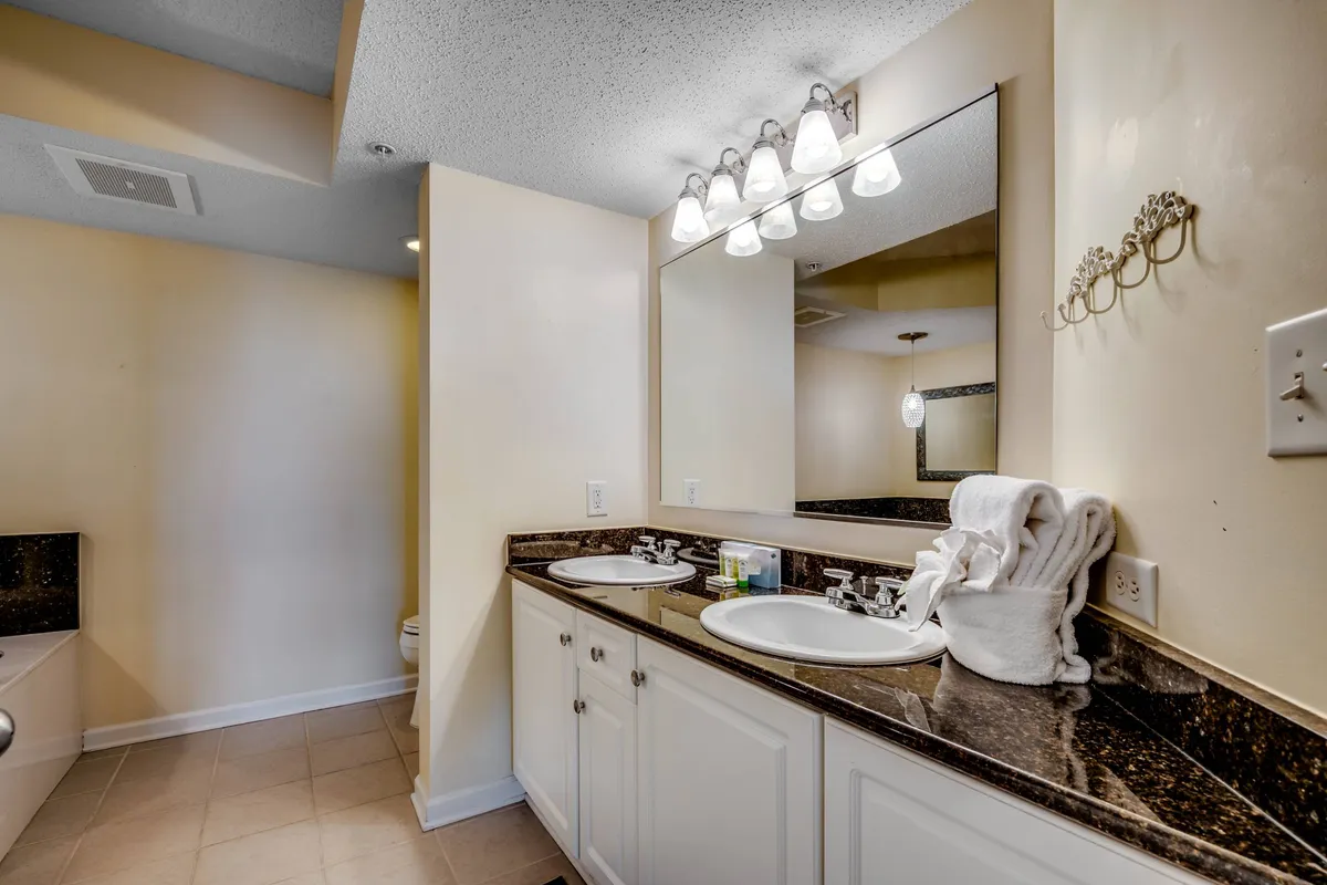 An elegant bathroom with dual sinks, a wide granite countertop, large mirror, and fresh towels neatly arranged. The organized and calm atmosphere invites guests to refresh and unwind as part of their private retreat.