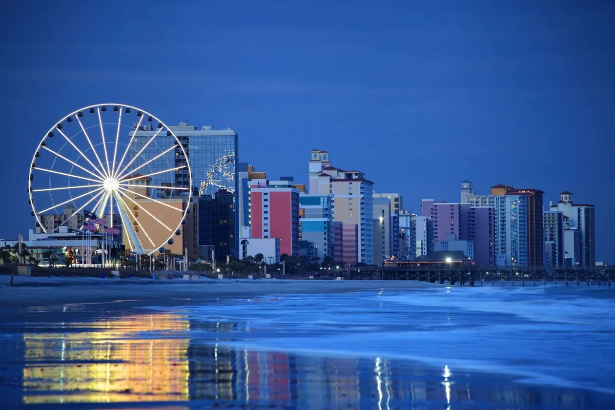 A vibrant exterior image featuring a Ferris wheel, lively colorful buildings, and the ocean reflecting the evening lights—a classic beachside amusement setting.