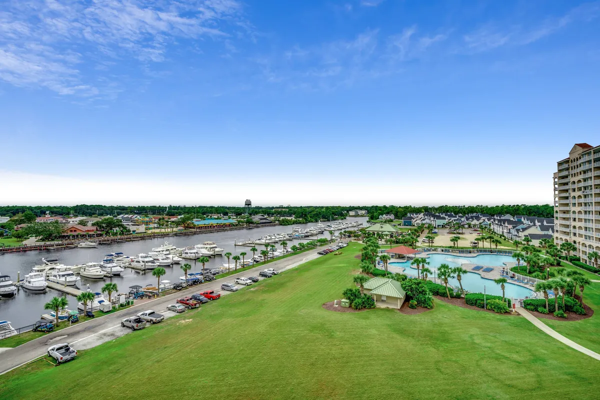 This image presents a sweeping view of the resort’s marina, a sparkling swimming pool surrounded by palm trees, a lush green lawn, and residential buildings in the background. Boats are docked at the marina, and the scene exudes a calm, inviting atmosphere perfect for outdoor recreation and relaxation.