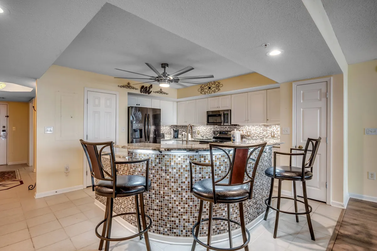 A welcoming view of the dining area and kitchen island bar, featuring a mosaic backsplash, modern appliances, and seating for casual meals or gatherings. The island bar visually connects the kitchen and dining spaces, illustrating the seamless transition from cooking to communal dining.