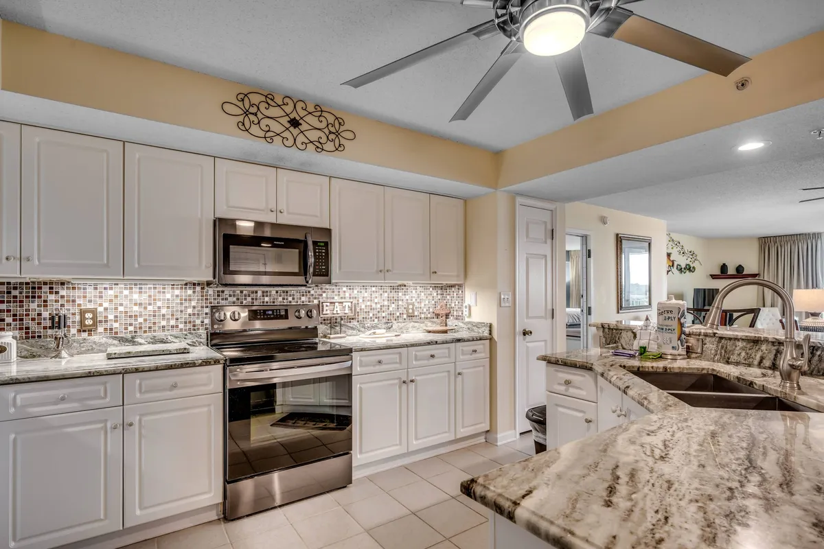 A bright, inviting kitchen with granite countertops, a kitchen island, stainless steel appliances including a fridge and dishwasher, and a colorful backsplash. The scene is set for cooking or casual dining, with a functional yet cheerful atmosphere that encourages both group meal prep and relaxed family breakfasts.