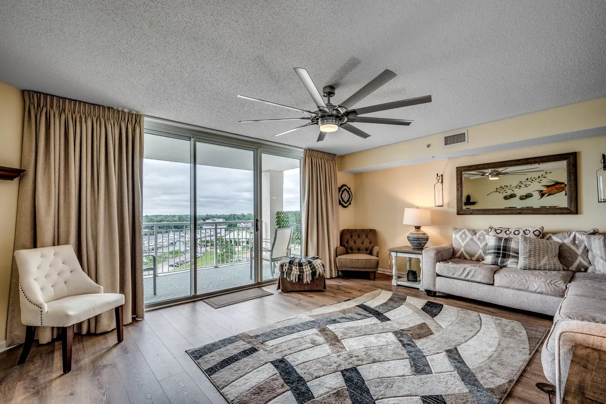 A cozy living area featuring a plush sofa adorned with decorative pillows, a stylish area rug, a modern lamp, and expansive sliding glass doors that open up to the outdoors, letting in ample natural light and offering a glimpse of water views.