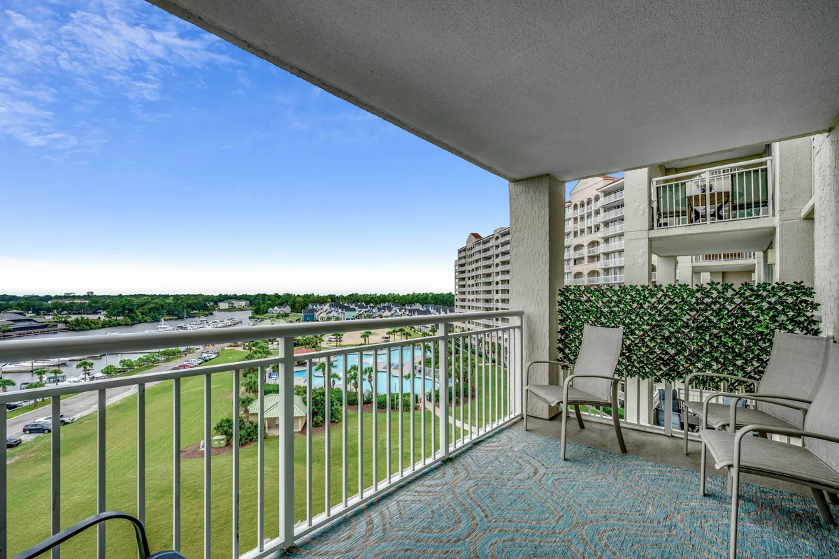 This exterior shot showcases a balcony view overlooking a pristine pool area and lush greenery, with a comfortable seating arrangement that invites guests to relax, sunbathe, or enjoy a drink. The open air and gentle breeze evoke the resort's vacation vibe and easy access to amenities.
