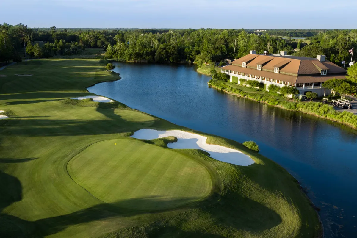 A picturesque golf course stretches out alongside a glistening water feature, with a clubhouse in the distance and sand traps adding definition to the green. The tranquil scene highlights the beauty and prestige of the resort’s golf offerings.